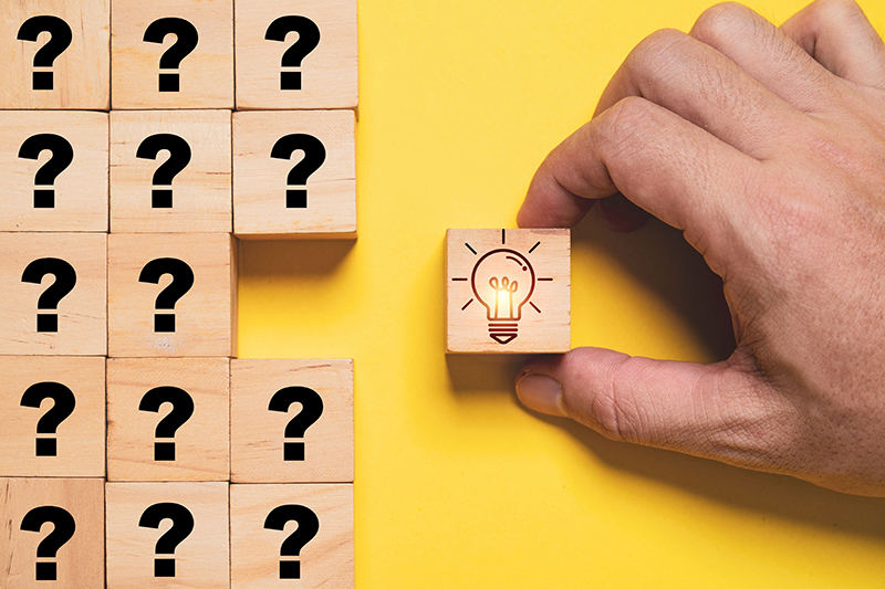 Glowing lightbulb illustration on a wooden block cube with question marks, symbolising creative thinking, idea generation, and problem-solving solutions.