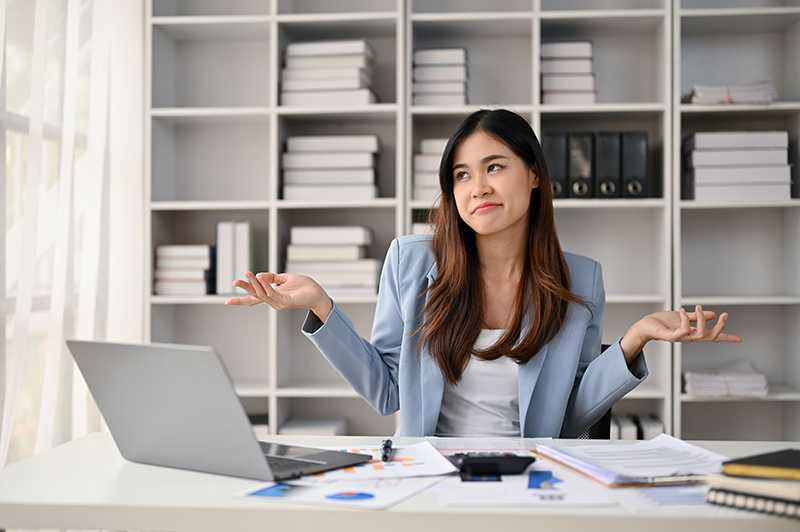 Woman sits at her office desk, shrugging her shoulders.