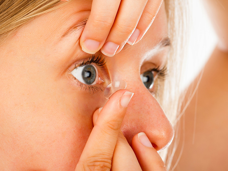 a picture of a woman inserting a contact lens