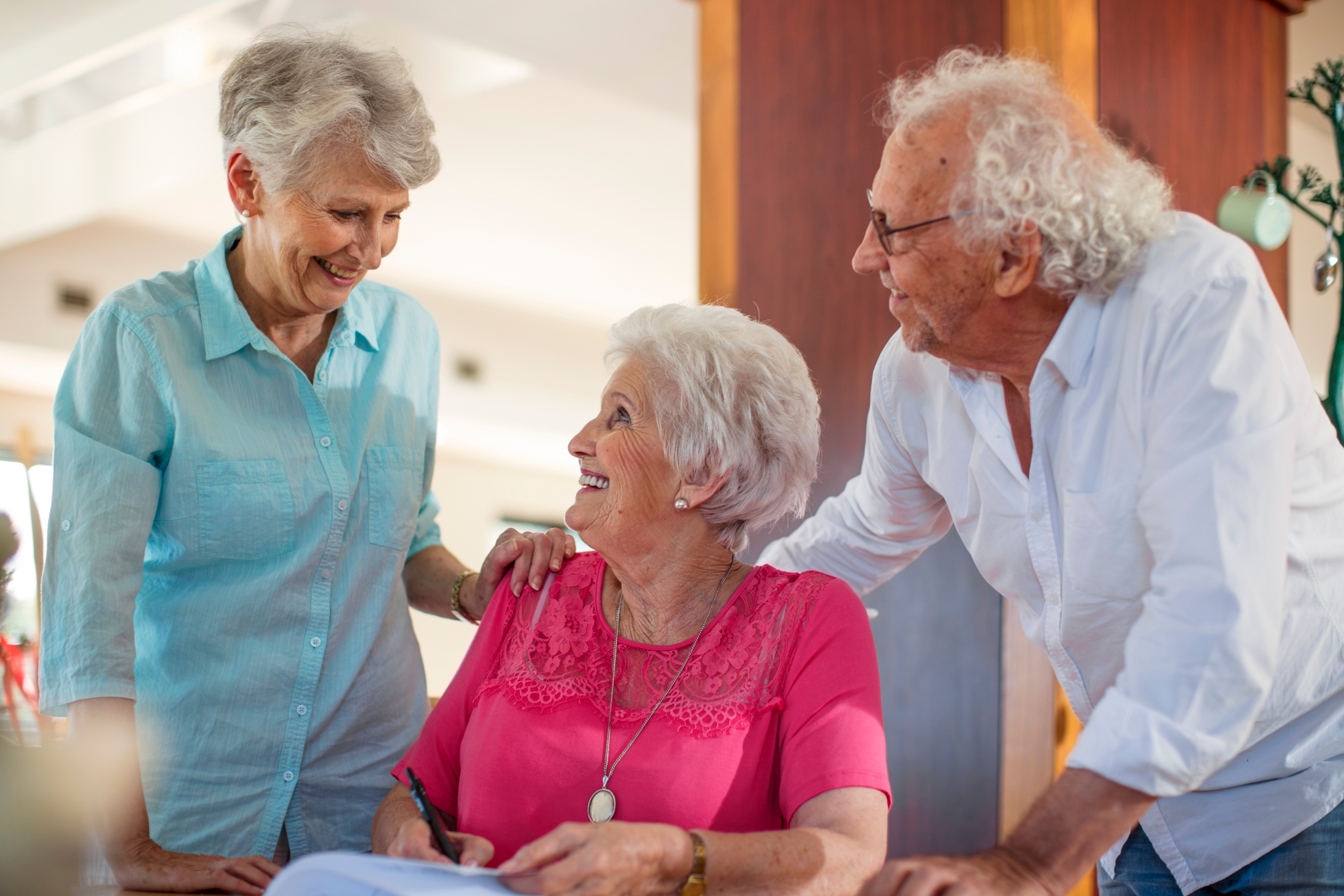 Senior woman signing a contract, friends reassuring her.