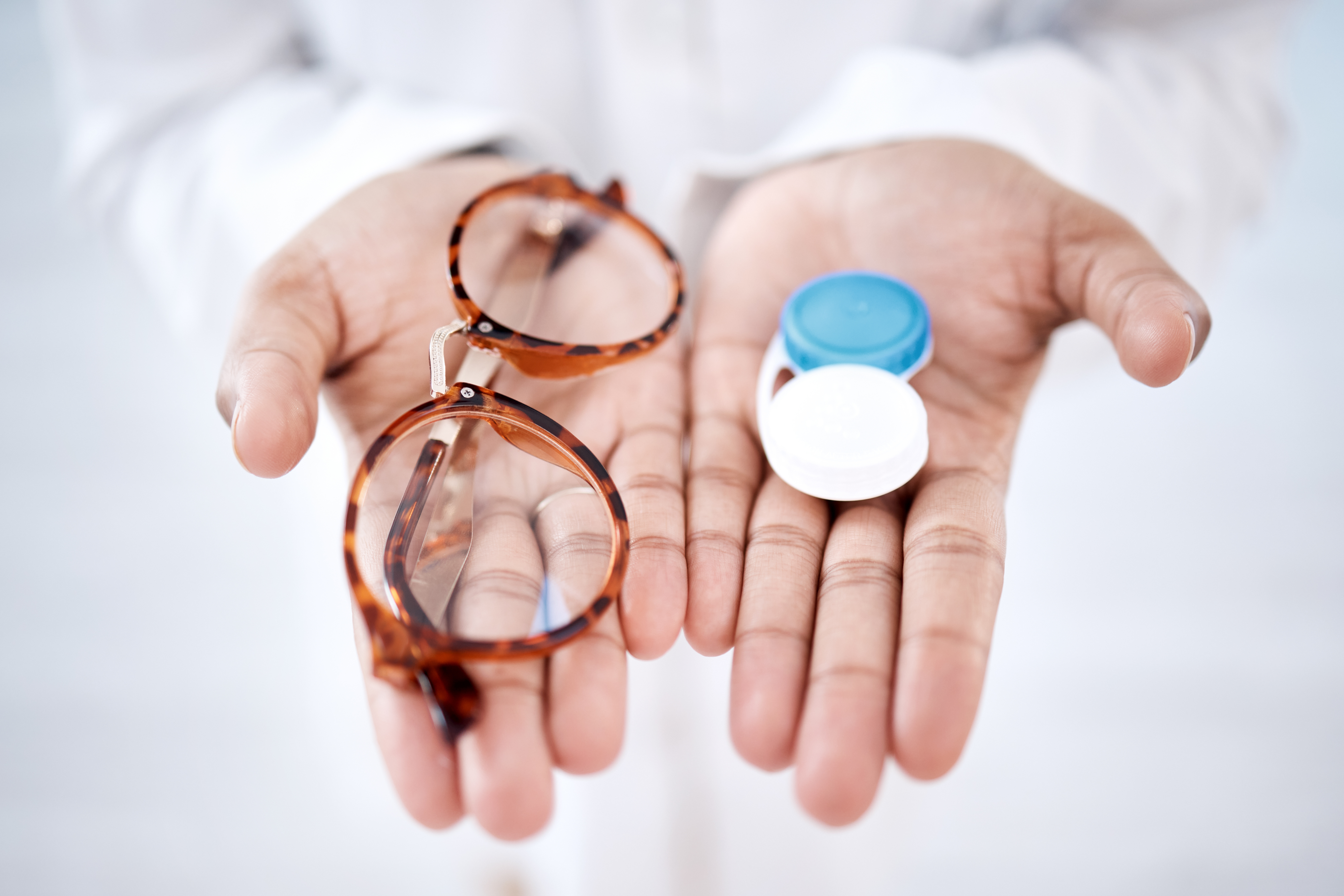 Person holding glasses and a contact lens container, illustrating eye care options and vision correction choices.