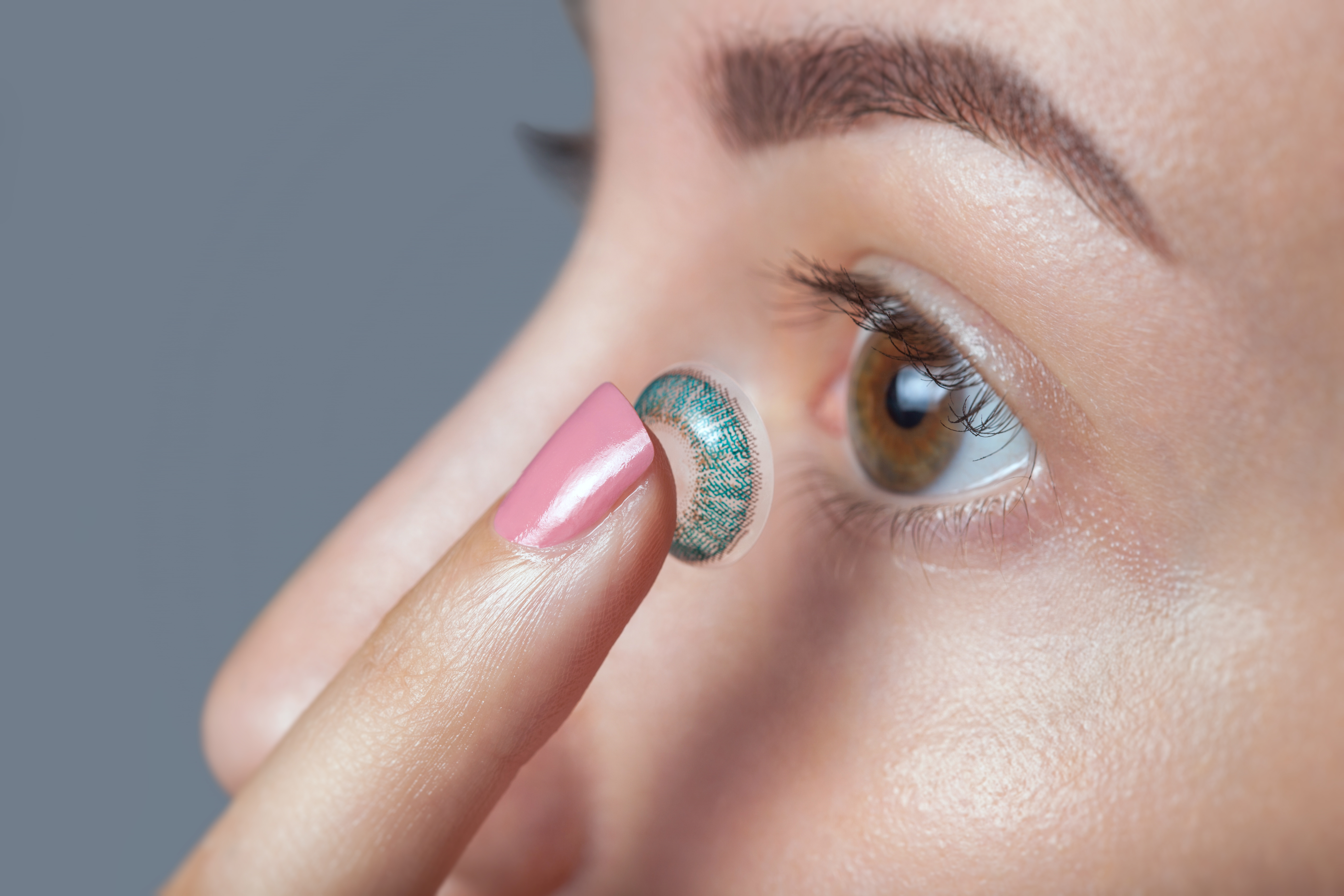 Woman holds a blue contact lens on her finger.