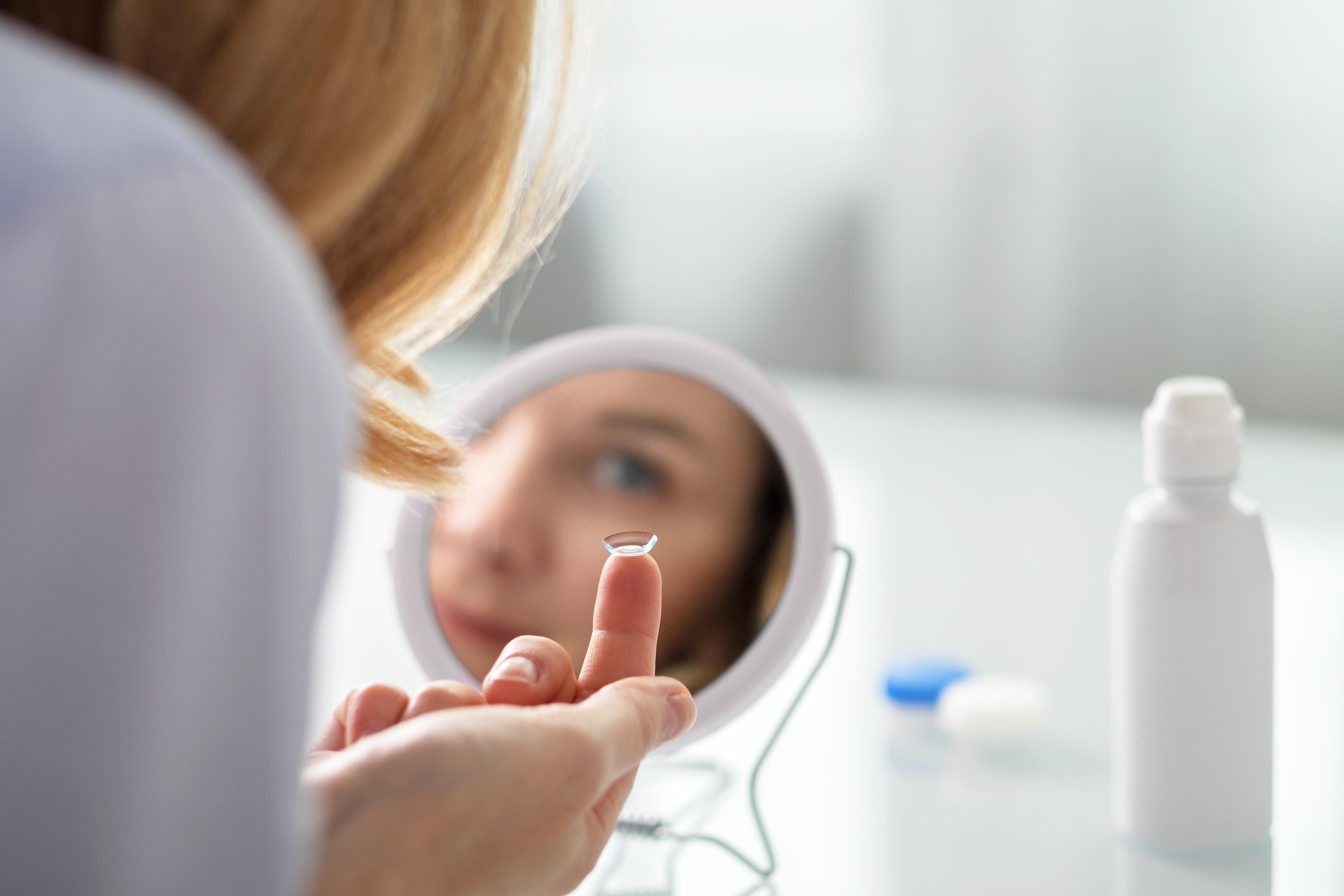 Woman putting in contact lenses in front of mirror.