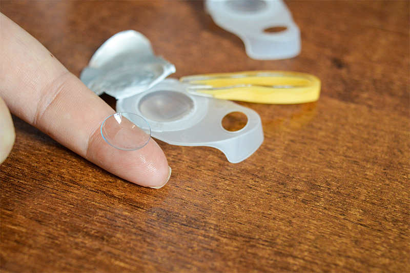soft contact lens balanced on fingertip with blister pack on the side.