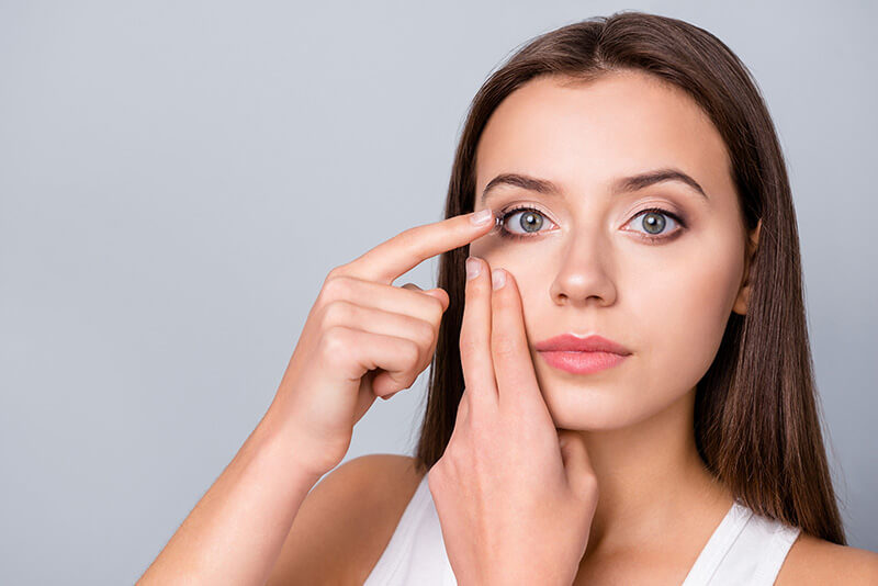 a picture of a woman inserting contact lenses into her eyes