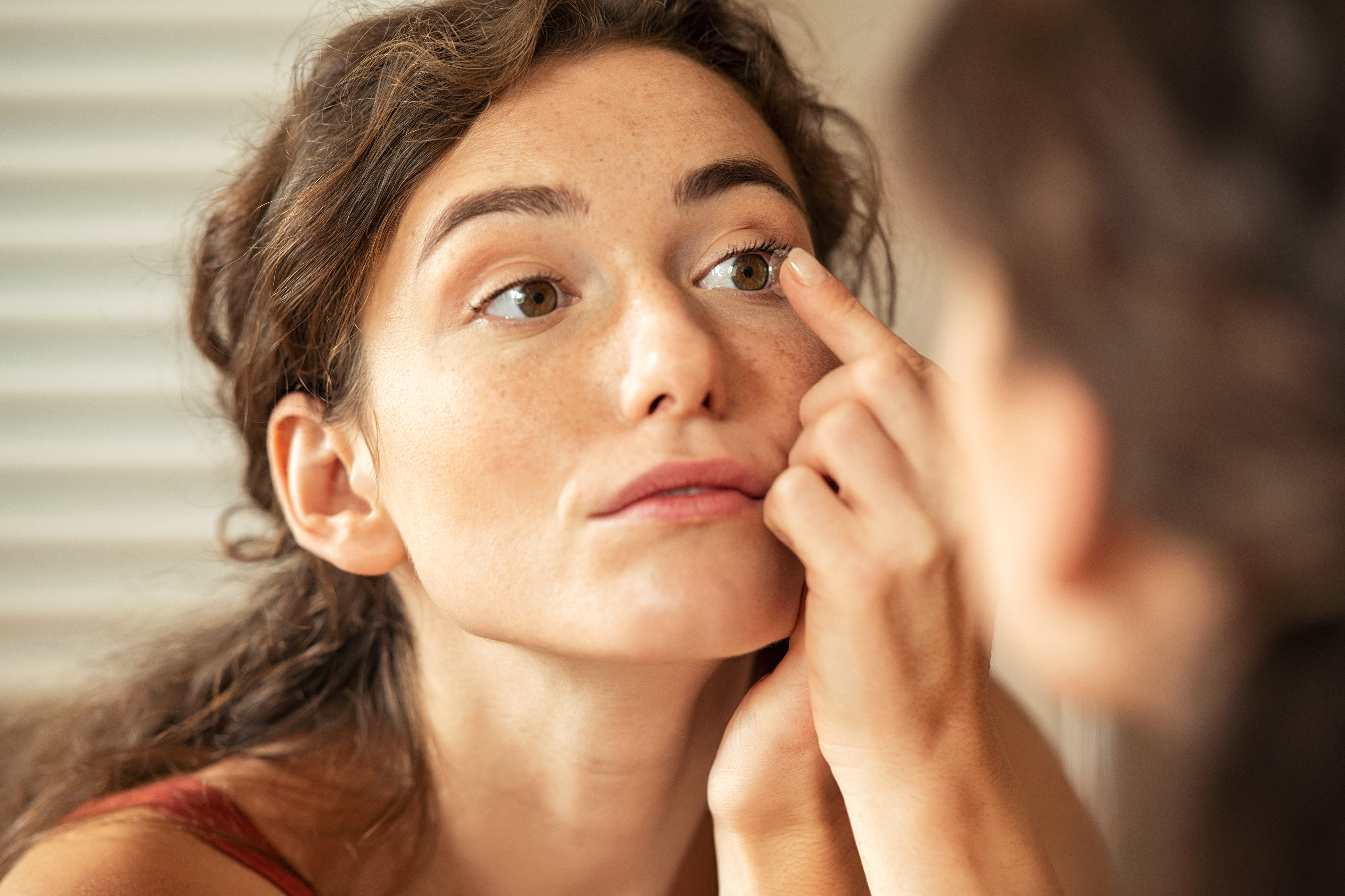 Woman applying contact lens in bathroom