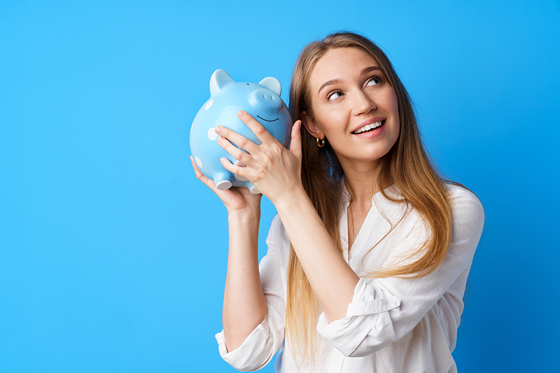 Woman holds piggy bank against blue background.