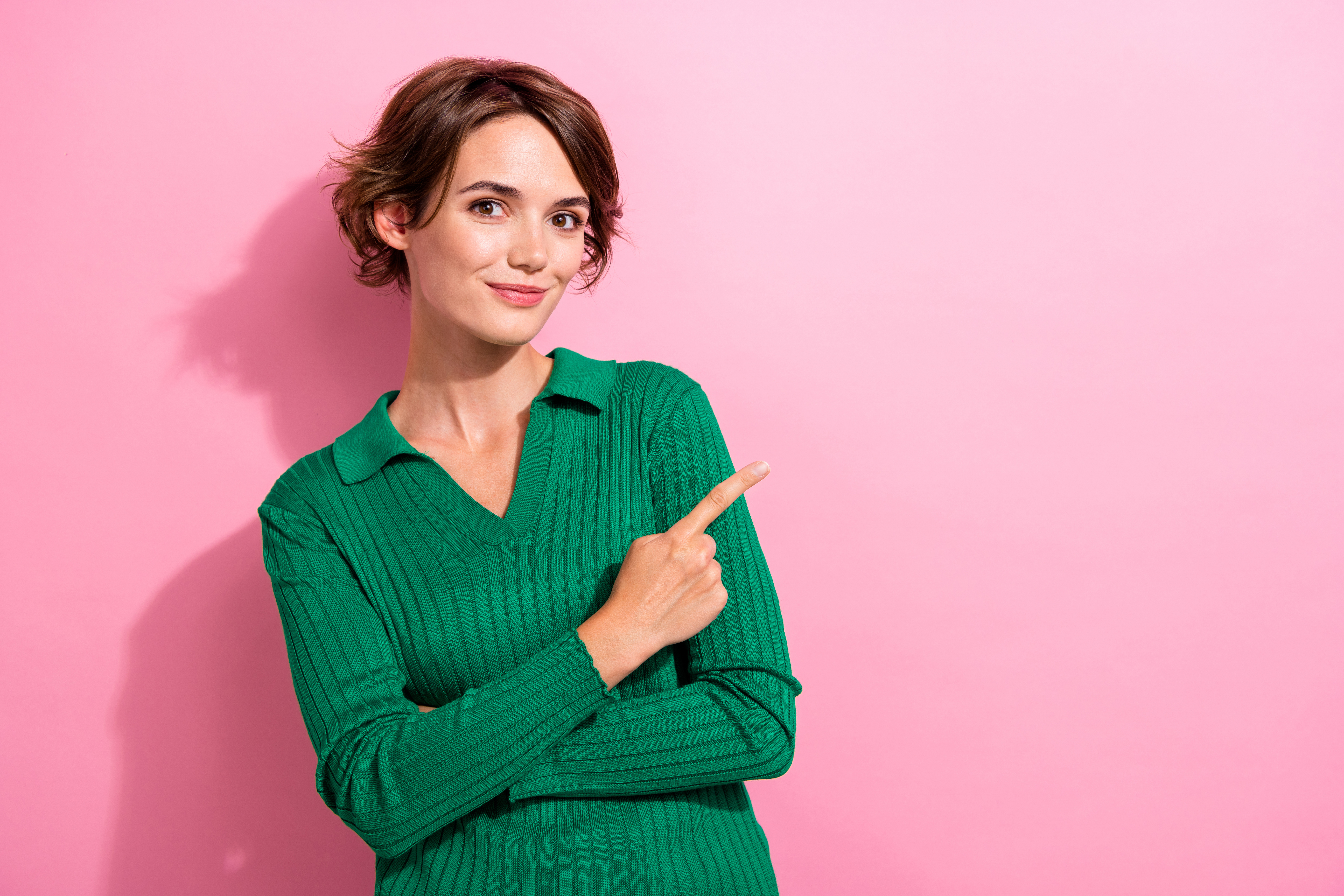 Woman pointing out with her forefinger against pink background.