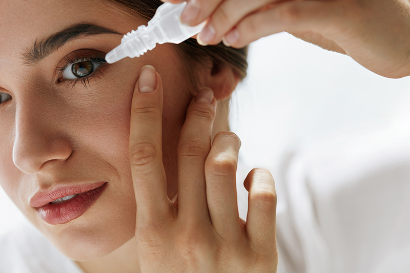 Woman applying eye drops into eye.