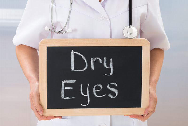 Blackboard with dry eyes written, held by someone wearing a white lab coat and stethoscope