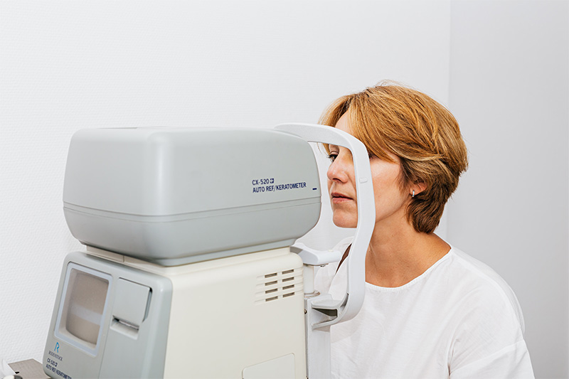 Dark blonde woman seated by eye testing machine, in middle of eye test