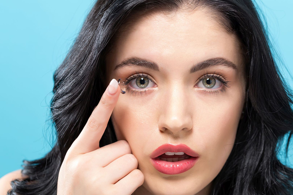 Close up of woman holding up contact lens to her right eye with index finger