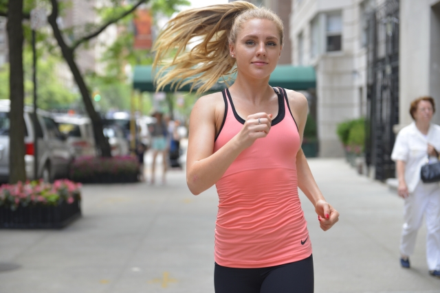 Blonde woman in pink singlet running through typical New York footpath