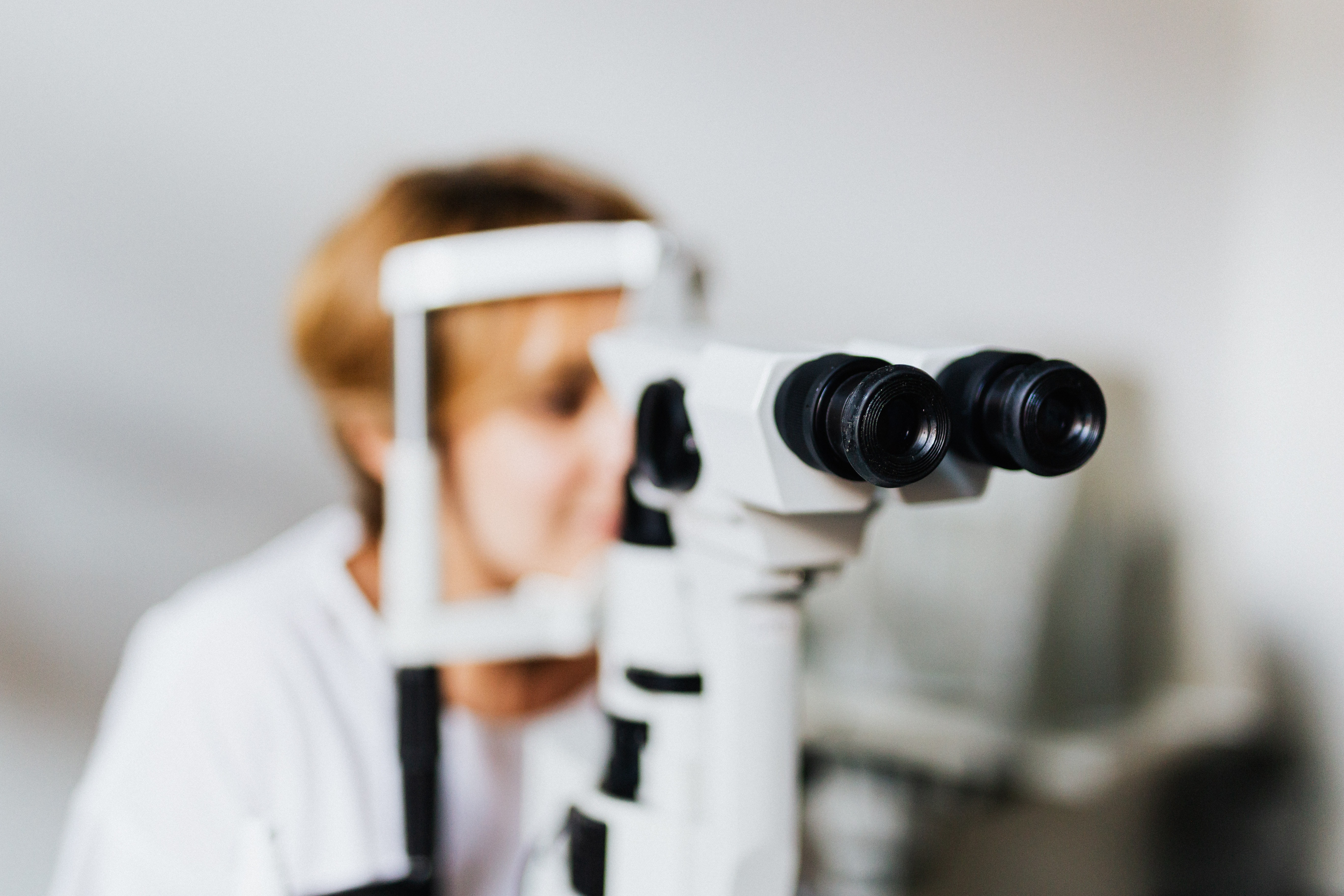 Women receiving eye test using white barrier around face with microscope eyepiece in forefront