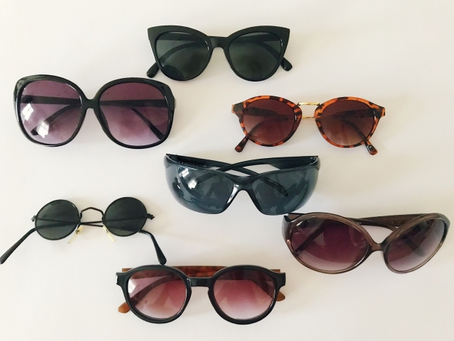 7 pairs of sunglasses of varying sizes and designs on a cream background