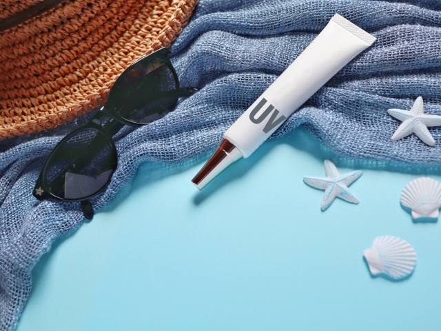 Blue towel, black sunglasses, straw hat, white unbranded sunscreen and seashells. starfish on a blue background